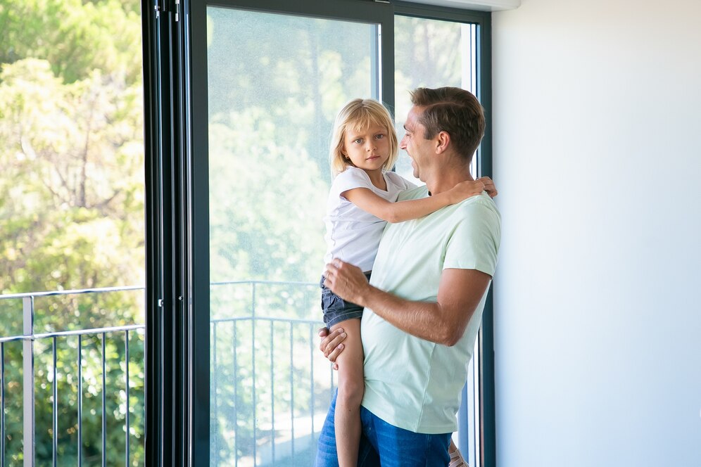 Padre cargando a su hija junto a ventana grande