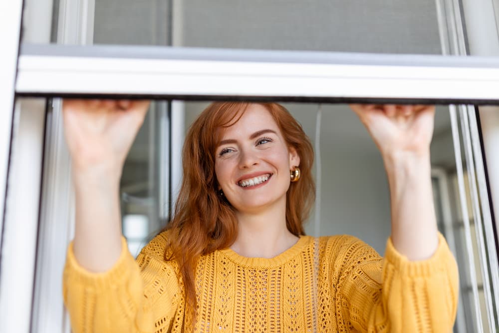 Mujer cerrando ventana con mosquiteras